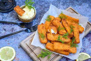 Close up of   Crispy breaded  deep fried fish fingers with breadcrumbs served  with remoulade sauce and  lemon Cod Fish Nuggets on rustic wood table background