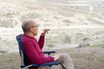 Man sitting on folding chair, drinking wine, relaxing and admiring the beautiful views of nature.
