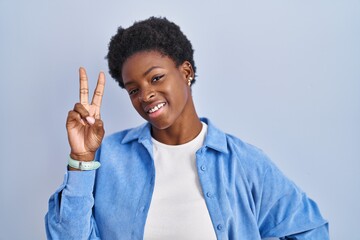 African american woman standing over blue background smiling looking to the camera showing fingers doing victory sign. number two.