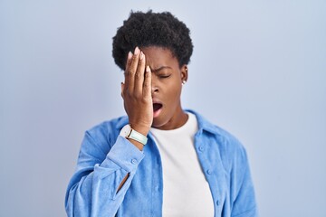 African american woman standing over blue background yawning tired covering half face, eye and mouth with hand. face hurts in pain.