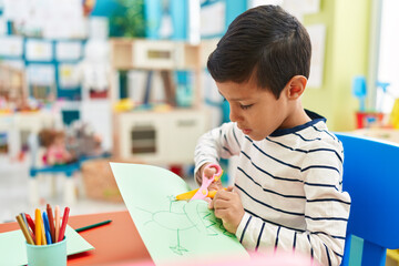 Adorable hispanic boy student cutting paper at kindergarten