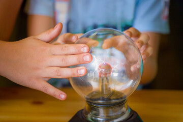 close-up of childrens hands putting their fingers on a glass ball with electrostatic discharge