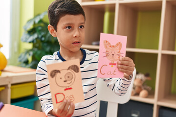 Adorable hispanic boy preschool student sitting on table showing cat and dog draw at kindergarten