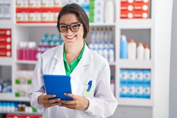 Young hispanic woman pharmacist smiling confident using touchpad at pharmacy