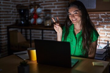 Young teenager girl working at the office at night smiling with happy face winking at the camera...