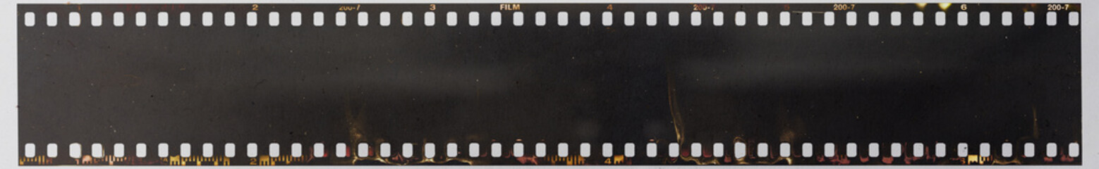 real macro photo of long 35mm filmstrip under dirty glass plate on white paper background. film...