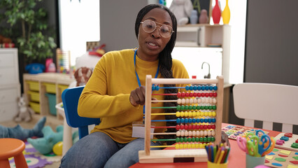 African woman working as teacher teaching maths with abacus at kindergarten