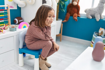 Adorable hispanic girl sitting on chair with relaxed expression at kindergarten