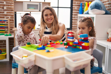 Fototapeta premium Teacher with girls playing with construction blocks sitting on table at kindergarten