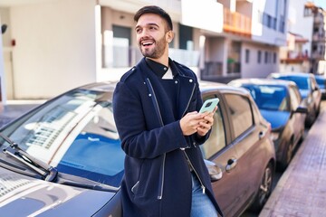 Young hispanic man using smartphone leaning on car at street