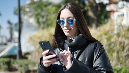 Young beautiful hispanic woman smiling confident using smartphone at park