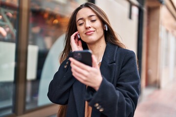 Young beautiful hispanic woman listening to music standing at street