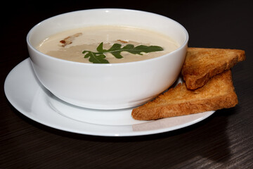 Cream cheese soup with croutons, white bowl, dark wooden background