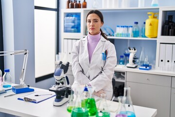 Fototapeta premium Young brunette woman working at scientist laboratory with serious expression on face. simple and natural looking at the camera.