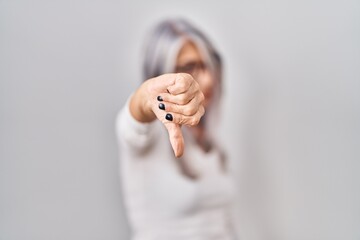 Middle age woman with grey hair standing over white background looking unhappy and angry showing...