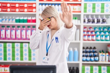 Young caucasian woman working at pharmacy drugstore covering eyes with hands and doing stop gesture with sad and fear expression. embarrassed and negative concept.