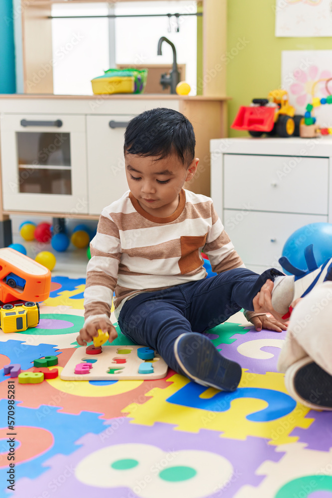 Wall mural Adorable hispanic toddler playing with maths puzzle game sitting on floor at kindergarten