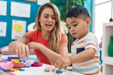 Teacher and toddler playing with geometry blocks sitting on table at kindergarten