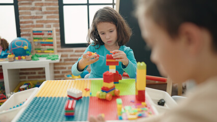 Two kids playing with construction blocks sitting on table at kindergarten