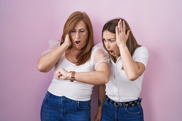 Hispanic mother and daughter wearing casual white t shirt over pink background looking at the watch time worried, afraid of getting late