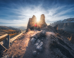 Woman on the mountain trail and stones at sunset in spring in Dolomites, Italy. Sporty girl on the path and high rocks. Colorful landscape with cliffs, stones, blue sky. Trekking and hiking. Travel