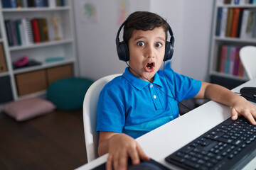 Little hispanic boy using computer laptop at the school scared and amazed with open mouth for...