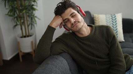 Young hispanic man listening to music relaxed on sofa at home