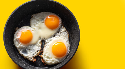 Frying pan with scrambled eggs from 3 eggs on a yellow background