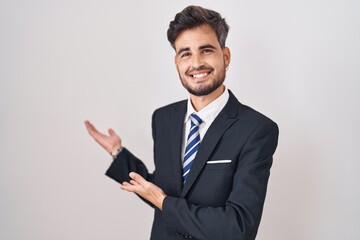 Young hispanic man with tattoos wearing business suit and tie inviting to enter smiling natural...