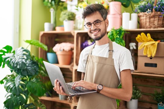 Young hispanic man florist smiling confident using laptop at flower shop