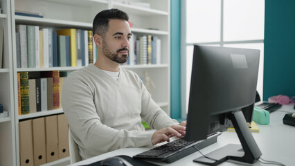 Young hispanic man student using computer studying at library university