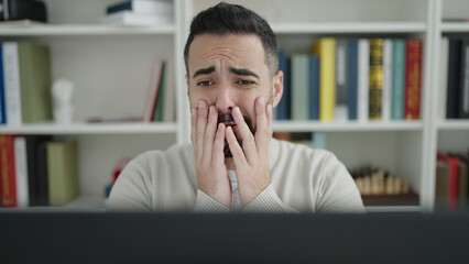 Young hispanic man student using computer stressed at library university