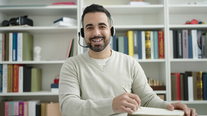 Naklejka premium Young hispanic man student having video call writing on notebook at library university