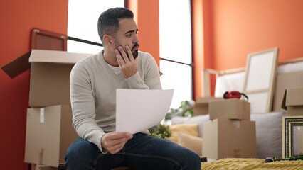 Young hispanic man sitting on sofa reading document at new home