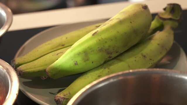 Slow motion green cooking bananas on the kitchen table. Fried plantain tostones popular dish of Latin America
