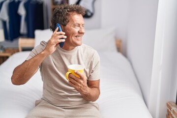 Middle age man talking on smartphone drinking coffee at bedroom