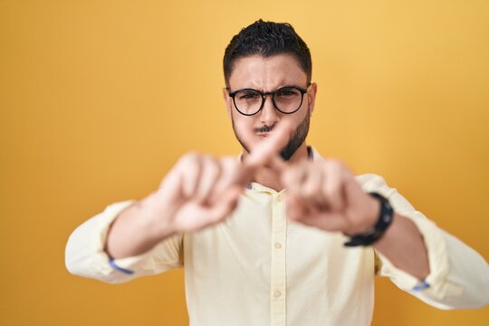 Hispanic young man wearing business clothes and glasses rejection expression crossing fingers doing negative sign