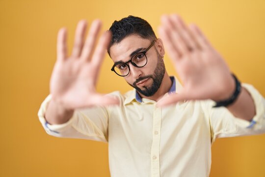 Hispanic young man wearing business clothes and glasses doing frame using hands palms and fingers, camera perspective