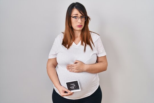 Pregnant woman holding baby ecography skeptic and nervous, frowning upset because of problem. negative person.