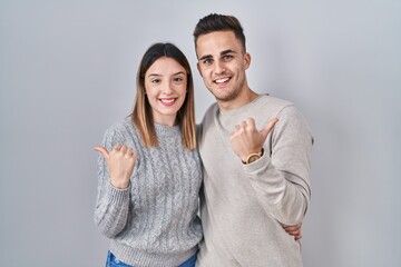 Young hispanic couple standing over white background pointing to the back behind with hand and thumbs up, smiling confident