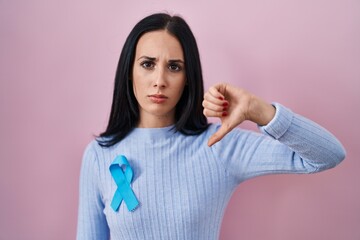 Hispanic woman wearing blue ribbon with angry face, negative sign showing dislike with thumbs down,...
