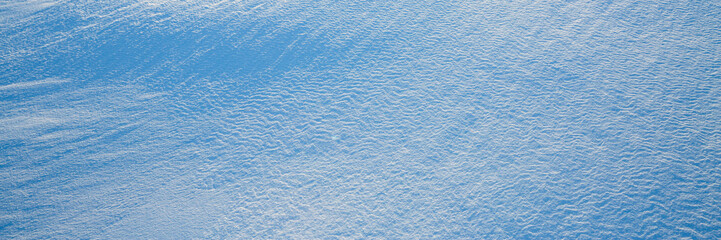 Beautiful winter background with snowy ground. Natural snow texture. Wind sculpted patterns on snow surface. Wide panoramic texture for background and design. Closeup top view with copy space.