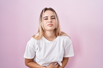Fototapeta premium Young blonde woman standing over pink background with hand on stomach because indigestion, painful illness feeling unwell. ache concept.
