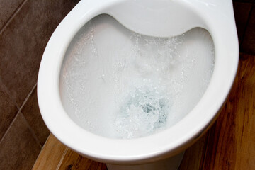 Toilet while flushing urine with water. A stream of water in the toilet bowl