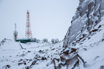 Winter landscape with a TV tower, antennas and satellite dishes on top of a snow-covered mountain.