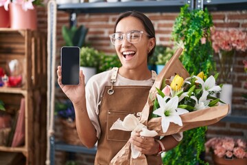 Young hispanic woman working at florist shop showing smartphone screen winking looking at the camera with sexy expression, cheerful and happy face.