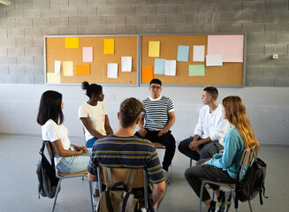 Group of multi-ethnic students sitting in a circle in a classroom while talking