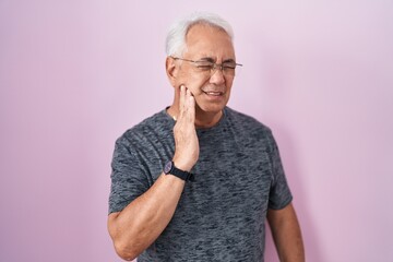 Middle age man with grey hair standing over pink background touching mouth with hand with painful expression because of toothache or dental illness on teeth. dentist