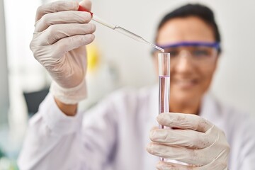 Middle age hispanic woman wearing scientist uniform using pipette at laboratory