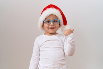 Little hispanic boy wearing glasses and christmas hat pointing thumb up to the side smiling happy with open mouth